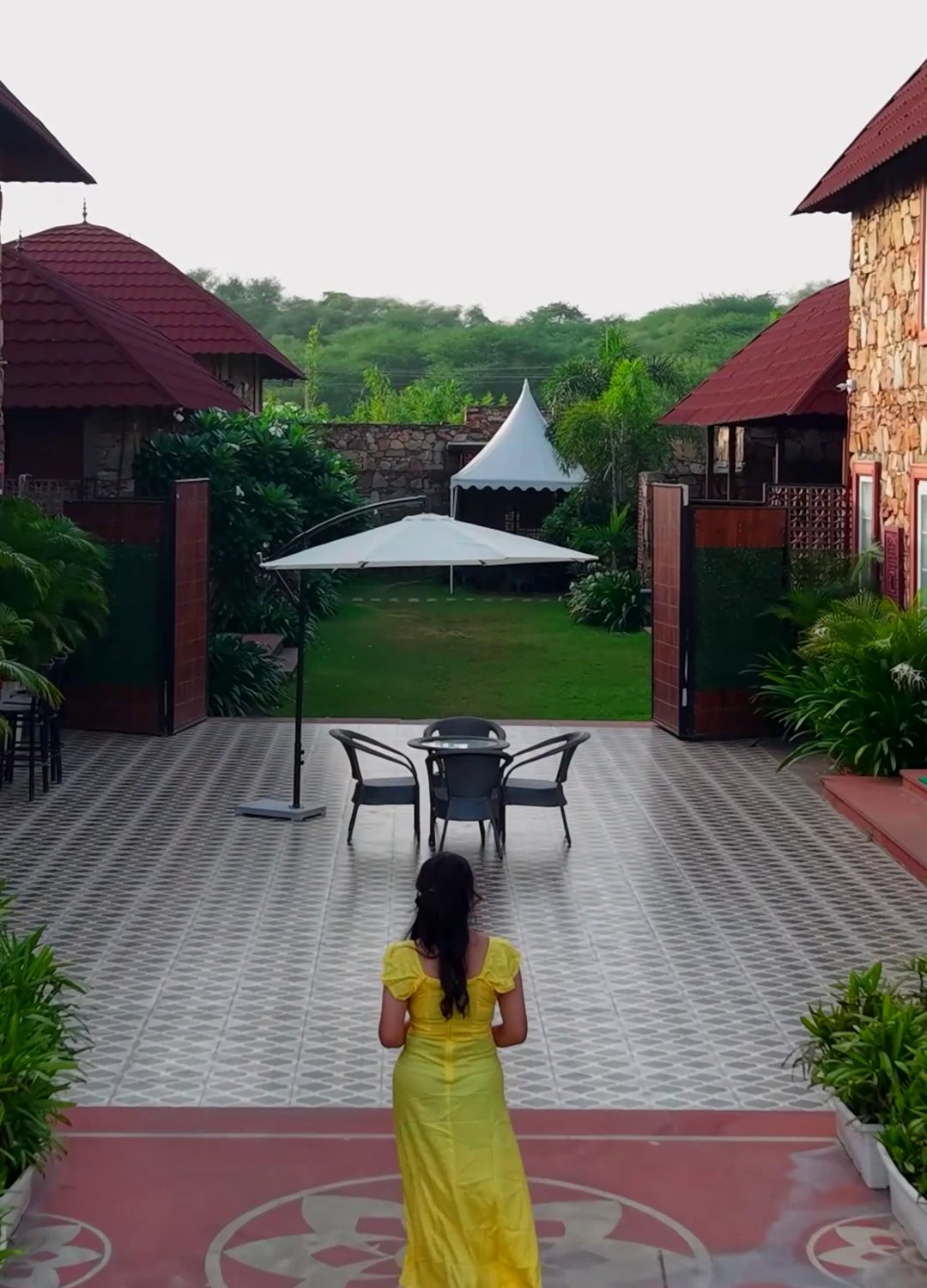 A guest walks across Qila's tiled courtyard towards the garden, clay-roofed villas and the Aravalli hills