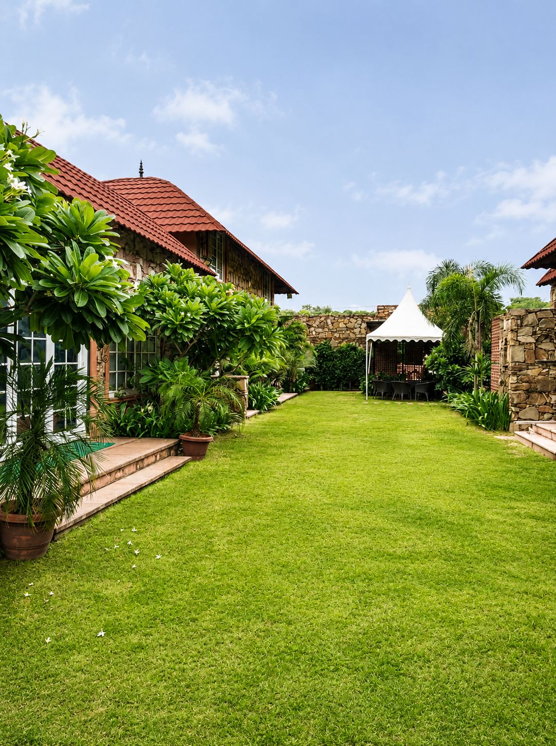 Wide lawn between the villa and the boundary wall, with a white gazebo